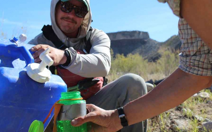 an outward bound student pours water from a jug into another student's water bottle